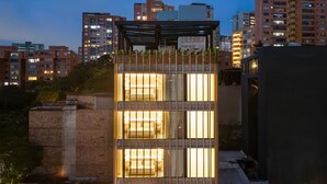 Un edificio moderno con varias habitaciones iluminadas, rodeado de otros rascacielos.
