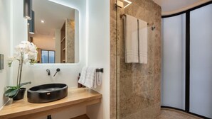 Un baño moderno con tocador de madera, un lavabo redondo, un espejo y un box de ducha de vidrio.