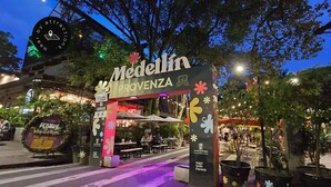 Un espacio al aire libre de noche con un cartel que dice 'Medellin Provence' y una decoración con motivos florales.