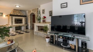 A living room with a stone fireplace, a large flat-screen TV, and a glass coffee table. - Villa Oaza - private pool, fitness, near a park forest (Pula)