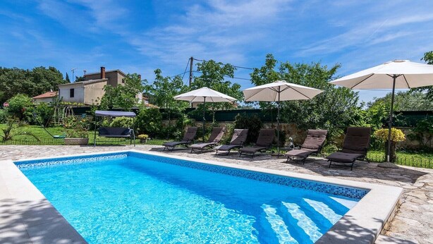 A rectangular swimming pool with clear blue water, surrounded by lounge chairs and umbrellas. - Villa Oaza - private pool, fitness, near a park forest (Pula)