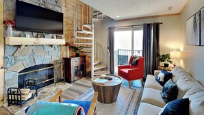 Ein Wohnzimmer mit Kamin aus Stein, einem roten Sessel, einer Couch und einer Treppe, die auf einen Balkon führt.