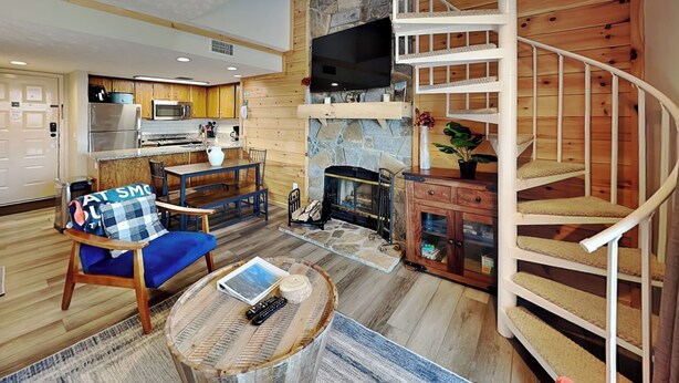 Ein modernes Wohnzimmer mit Kamin, einer Holztreppe und einer Küchenzeile mit Holzschränken und einer Mikrowelle.