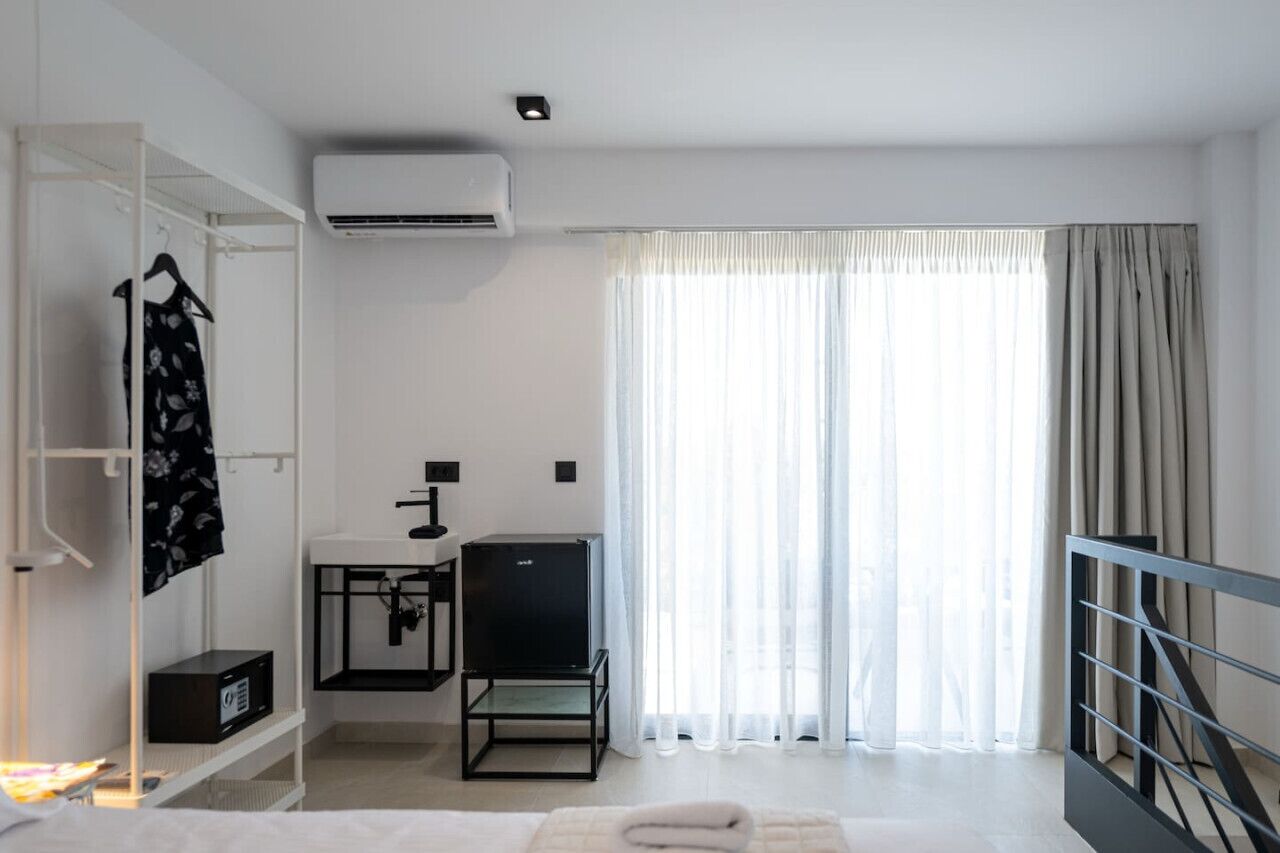 A modern hotel room with a bed, a desk with a chair, an air conditioner, and a wardrobe.