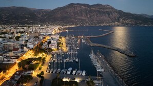 A marina with boats docked, a marina pier, and a cityscape with buildings and mountains in the background. - KEDL Junior Suites 302 (Kalamata)