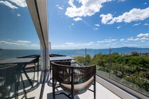 A balcony with wicker chairs and a table, overlooking a coastal view with clear skies. - KEDL Junior Suites 503 (Kalamata)