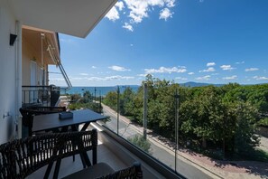 A balcony with a table and chairs, overlooking a road and greenery. - KEDL Junior Suites 503 (Kalamata)