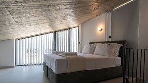 A bedroom with a large bed, a sloped ceiling, and a view through floor-to-ceiling windows. - KEDL Junior Suites 501 (Kalamata)