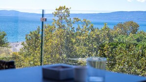 A table with a glass and a box, overlooking a scenic view of the sea and hills. - KEDL Junior Suites 501 (Kalamata)
