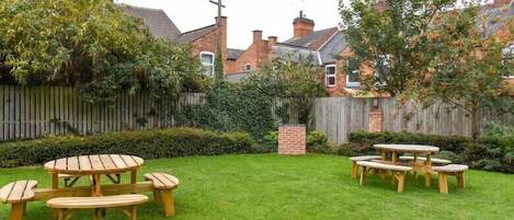 A backyard with a wooden picnic table and benches, surrounded by a wooden fence and greenery.