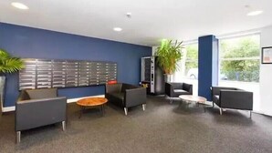 Un espace d’attente moderne avec des murs bleus, une grande plante et plusieurs options d’assises, notamment une table ronde et des chaises.