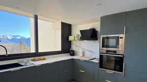 Una cocina moderna con armarios oscuros, microondas integrado y horno. Una ventana ofrece vistas a montañas.