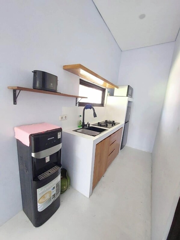 A compact kitchen with a built-in stove, a sink, and wooden cabinets. - Double D Guesthouse and Villa (Kerobokan)