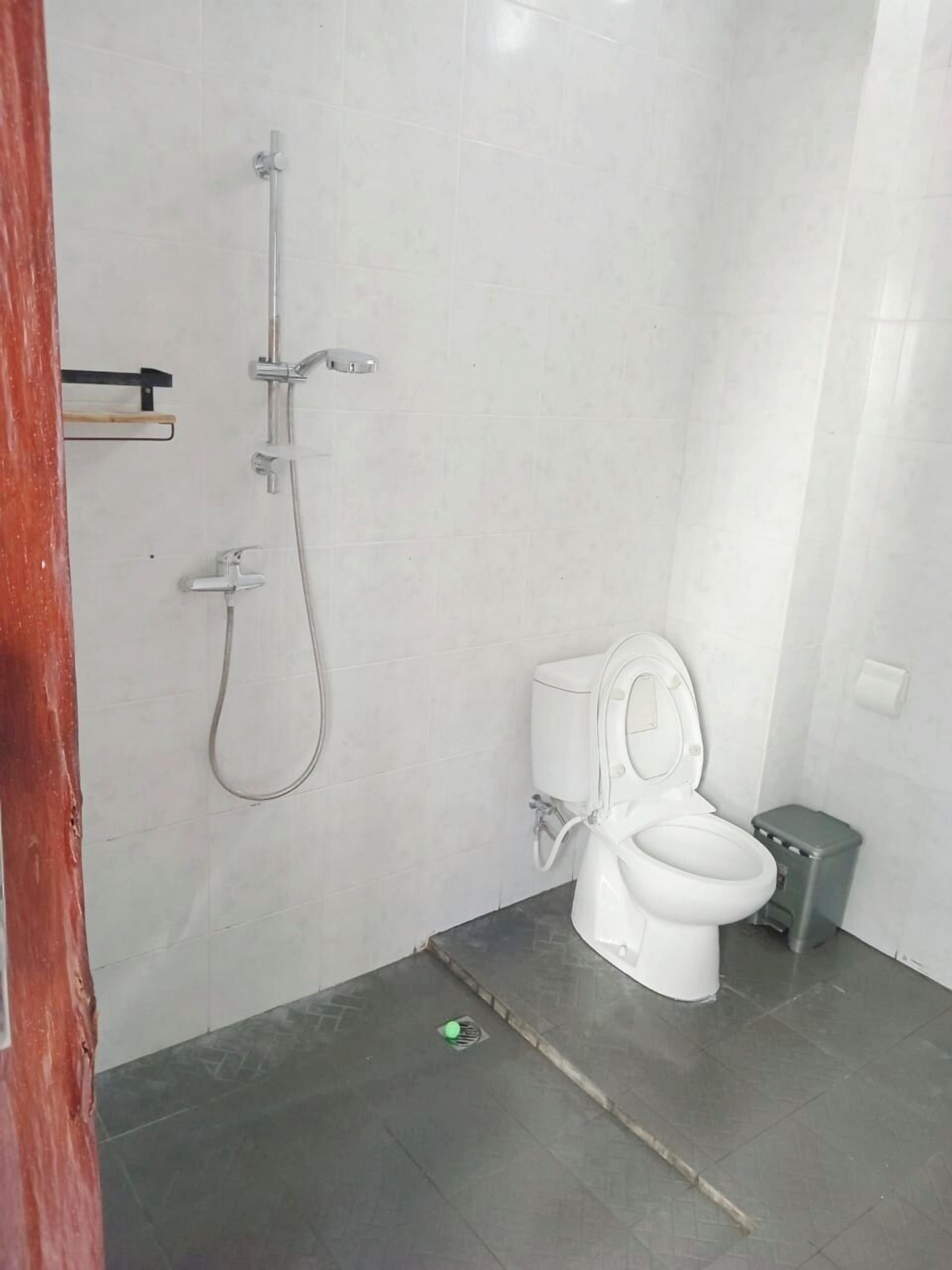 A small, clean bathroom with a toilet, a shower, and a trash bin.