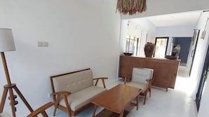 Una sala de estar moderna con sofá, mesa de centro y sillas de madera. Se observa una lámpara colgante.