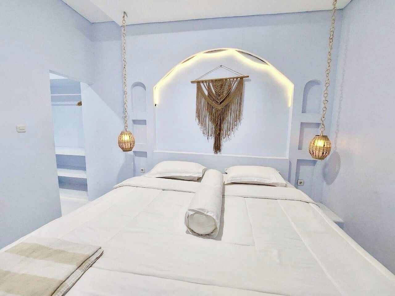 A bedroom with a large bed, a hanging light fixture, and a wall-mounted decorative piece.