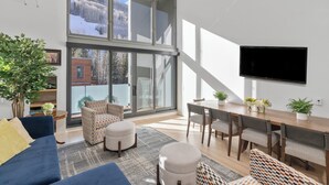 A modern living room with a large window, a flat-screen TV, and a dining area with a wooden table and chairs. - Spritz House- 4 Level Telluride Luxury with Penthouse (Telluride)