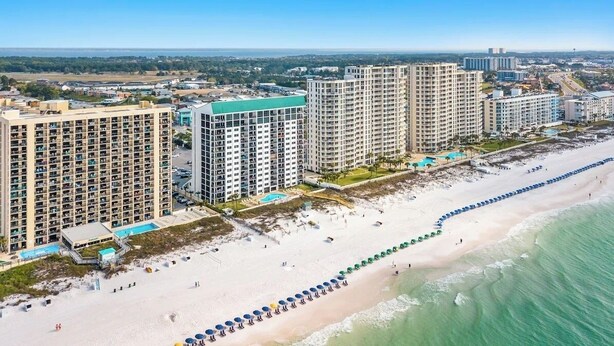 Ein Strandhotel mit mehreren Hochhäusern, einem Sandstrand und einer langen Reihe von Sonnenschirmen.