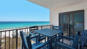 Ein Balkon mit Meerblick, einem Tisch, Stühlen und einer Glastür zu einem Schlafzimmer.