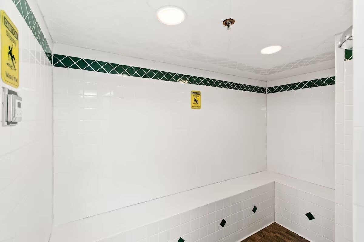 Un baño con paredes de azulejos blancos, un borde verde y blanco estampado y un letrero de precaución.
