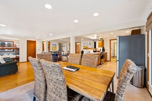 A spacious living area with a wooden dining table, wicker chairs, a sofa, and a kitchen in the background.