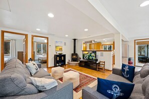 A modern living room with a sofa, ottoman, TV, fireplace, and kitchen area.