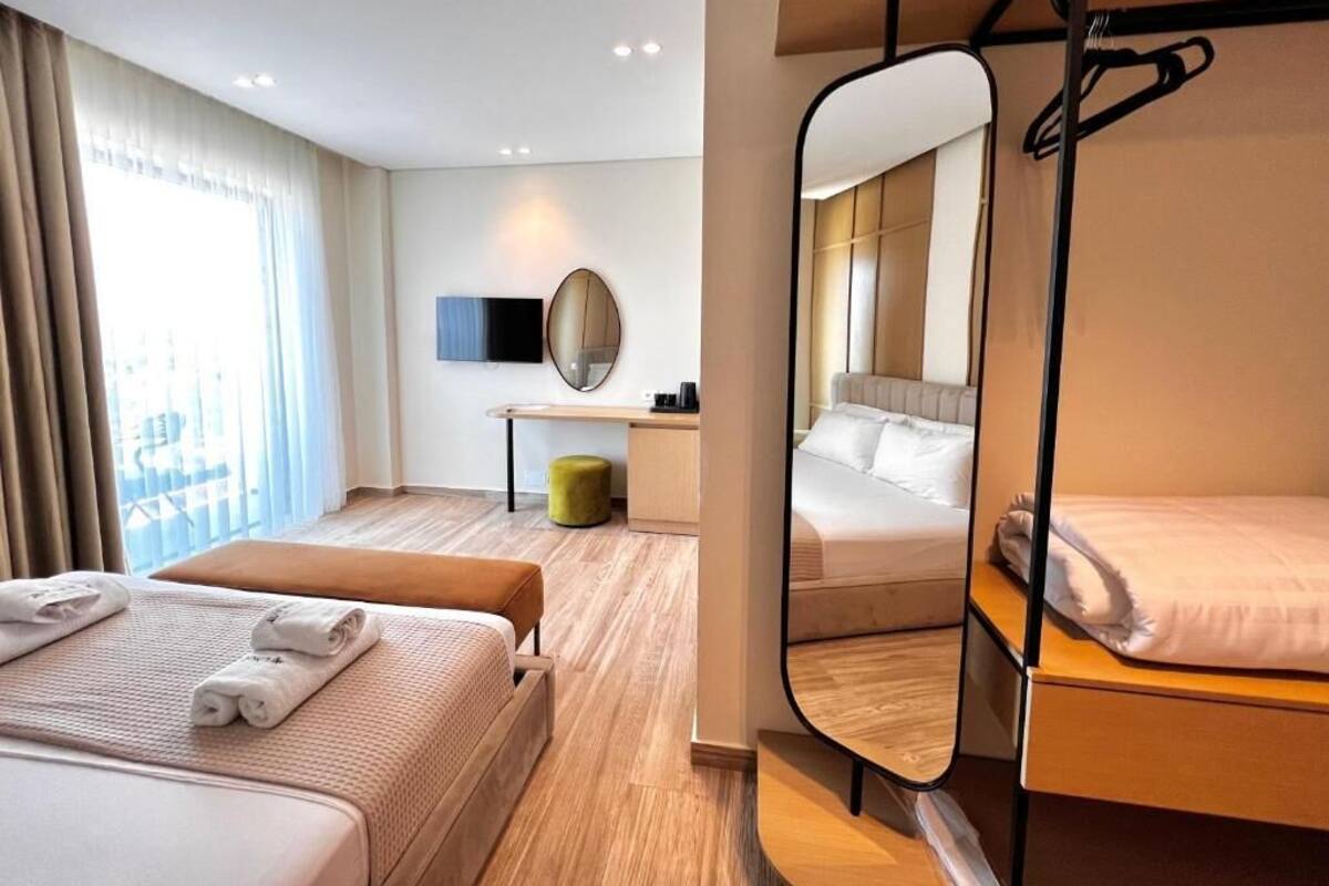 A hotel room with a bunk bed, a desk with a chair, a mirror, and a window with curtains.