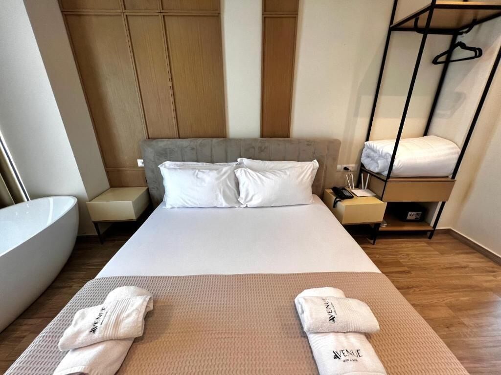 Hotellihuone, jossa on suuri sänky, yöpöytä, riipputuoli ja kylpyamme.