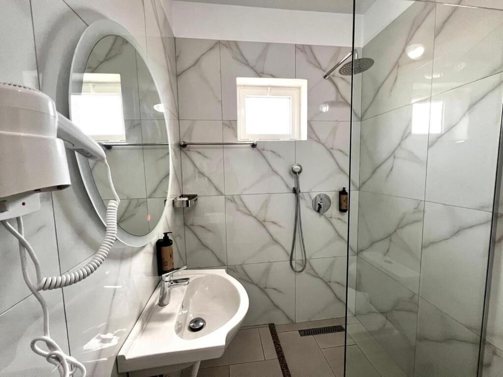 A bathroom with a marble wall, a pedestal sink, a handheld showerhead, and a hairdryer.