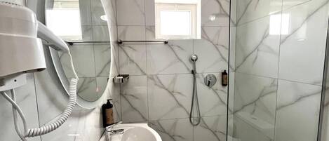 Un baño moderno con piso de mármol, un lavamanos, un cabezal de ducha de mano y un secador de pelo.