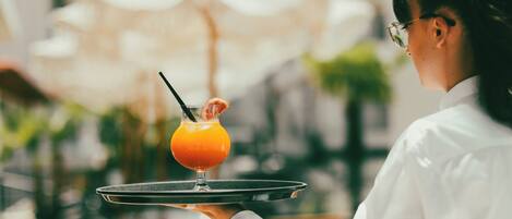 A person holding a tray with a glass of orange juice and a slice of orange.