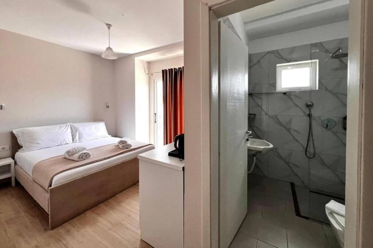 A bedroom with a bed, bedside table, and a bathroom with a shower, sink, and toilet.