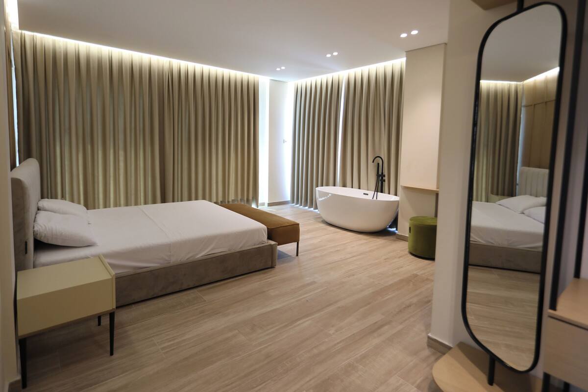 A modern bedroom with a large bed, a bathtub, and a mirror.