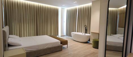 A modern bedroom with a large bed, a bathtub, and a mirror.