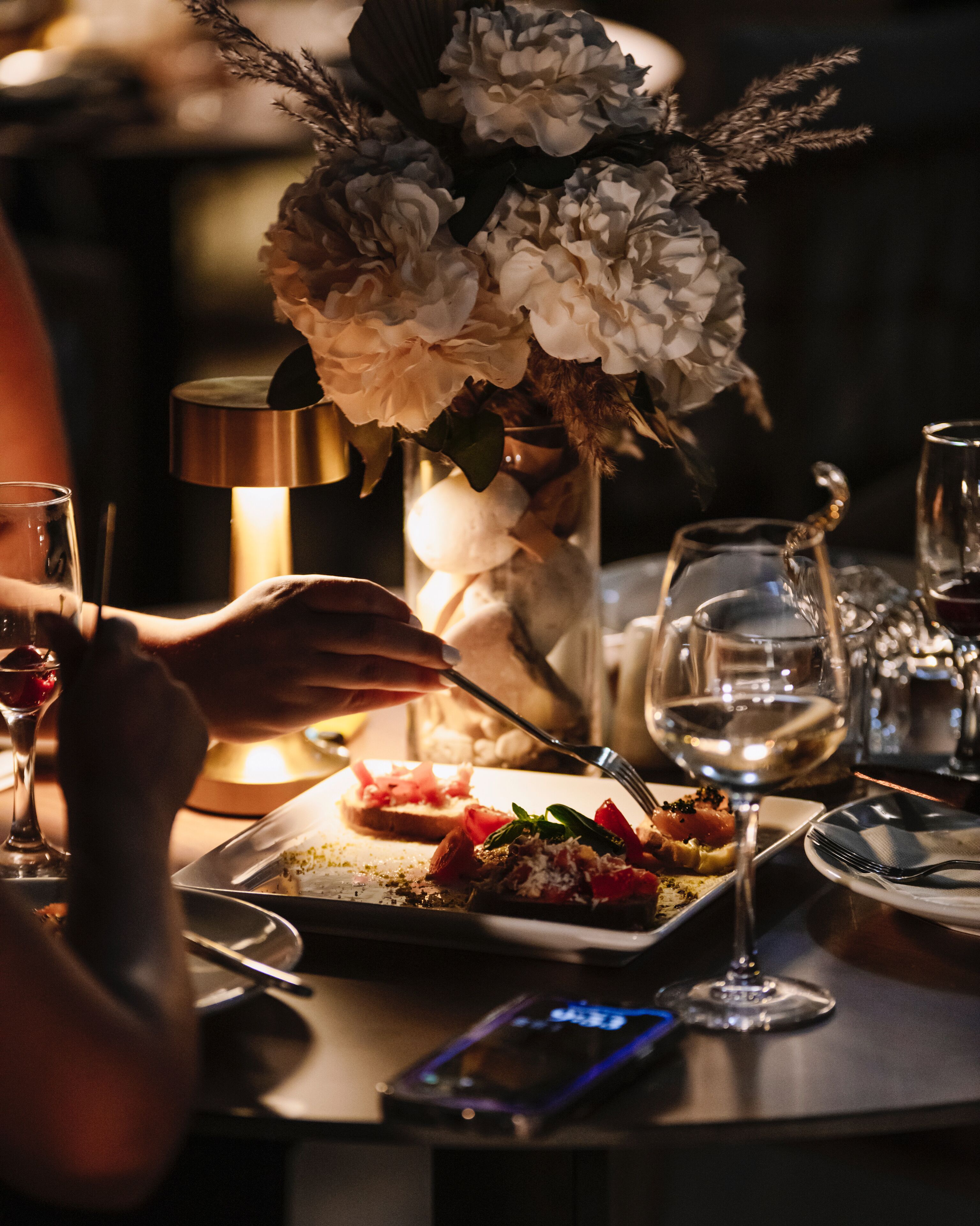 A dining table with a candle, a vase of flowers, and a plate of food.