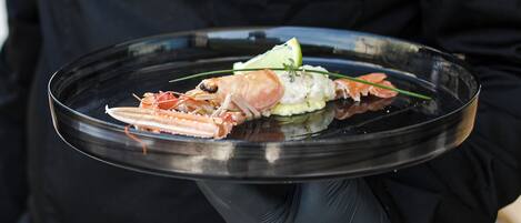 A person holding a clear glass plate with a lobster and garnishes.