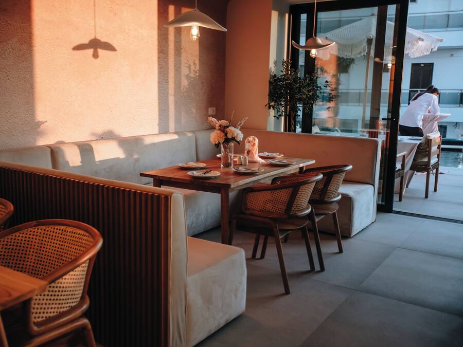 An outdoor seating area with wooden tables and chairs, a cushioned bench, and a glass partition.