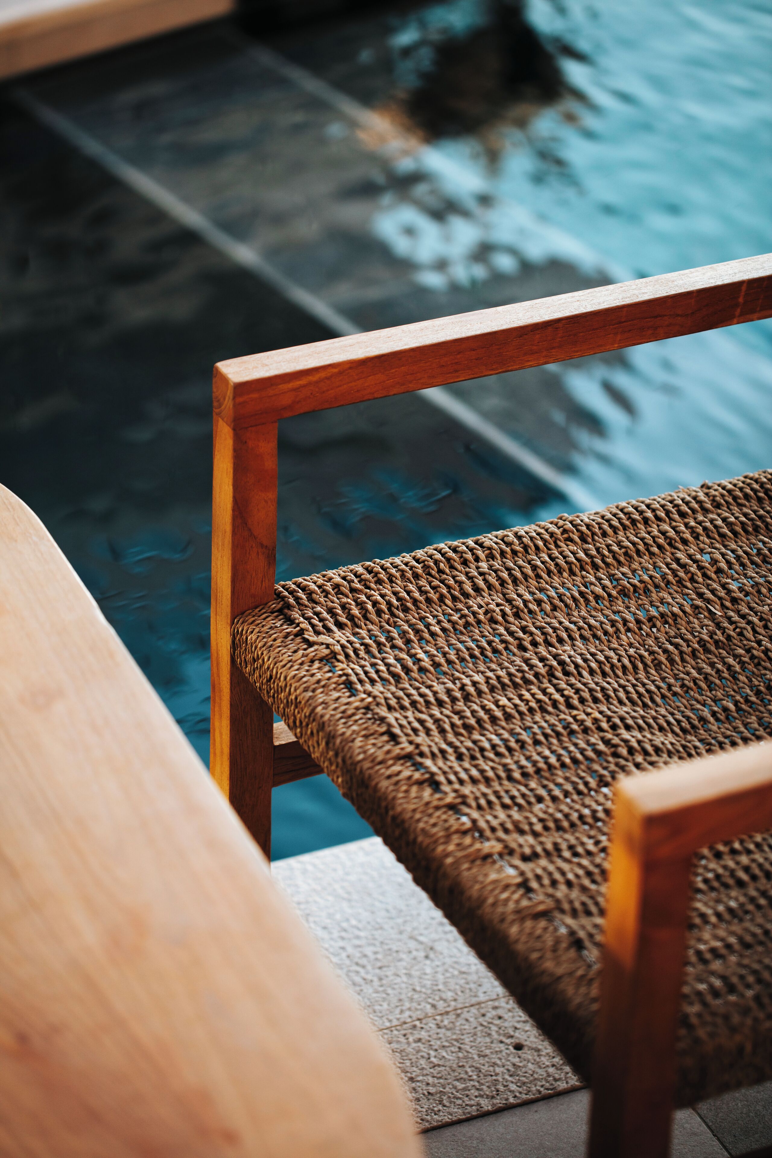 Una silla de madera con asiento de mimbre junto a una piscina.
