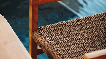 Una silla de madera con asiento de mimbre junto a una piscina.