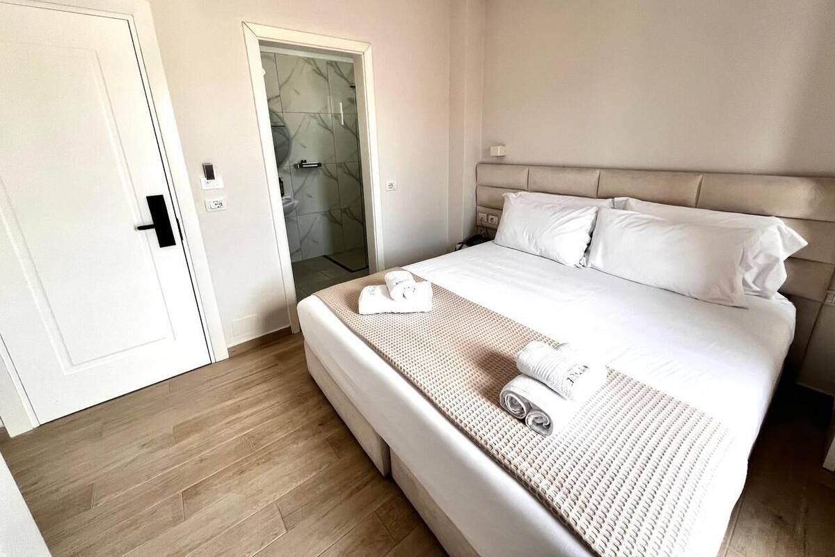 A hotel room with a bed, a door, and a bathroom with a glass shower.