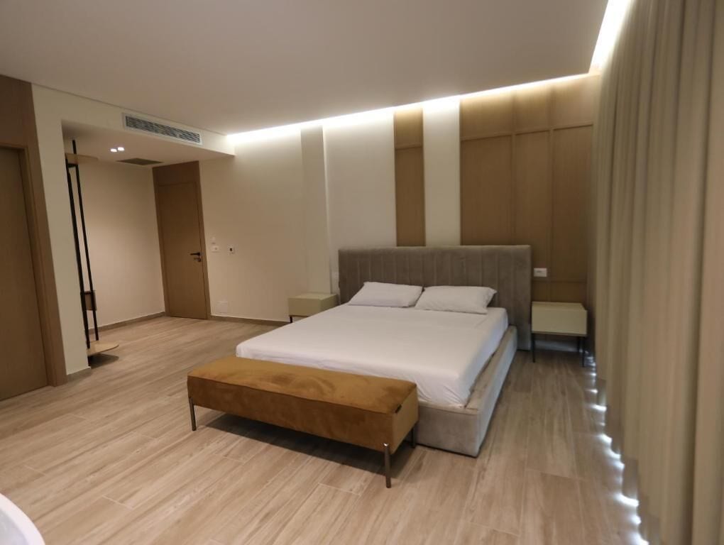Moderni hotellihuone, jossa on suuri sänky, penkki ja yöpöytä.