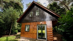 Una cabaña de madera rústica con techo inclinado, dos ventanas y un pequeño porche.