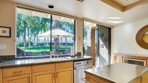 A kitchen with wooden cabinets, a stainless steel stove, and a view of a backyard with a patio umbrella. - Del Sol: Resort Style Living, BBQ, Fire Pit, Peace (Palm Desert)