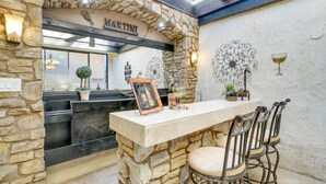 A stone-walled bar area with a 'Martini' sign, a chalkboard menu, and a framed picture. There are three metal chairs with cushioned seats. - Del Sol: Resort Style Living, BBQ, Fire Pit, Peace (Palm Desert)