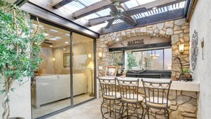 A bar area with stone walls, a Martini sign, and a glass-enclosed seating area with a sofa and a table. - Del Sol: Resort Style Living, BBQ, Fire Pit, Peace (Palm Desert)