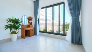 A spacious room with a large window, a wooden desk, a potted plant, and a mirror. - Ho Quy Ly Holiday Apartment for Family (Ho Chi Minh City)
