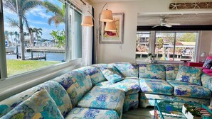 A living room with a large window overlooking a marina, a sectional sofa with floral upholstery, and a ceiling fan.