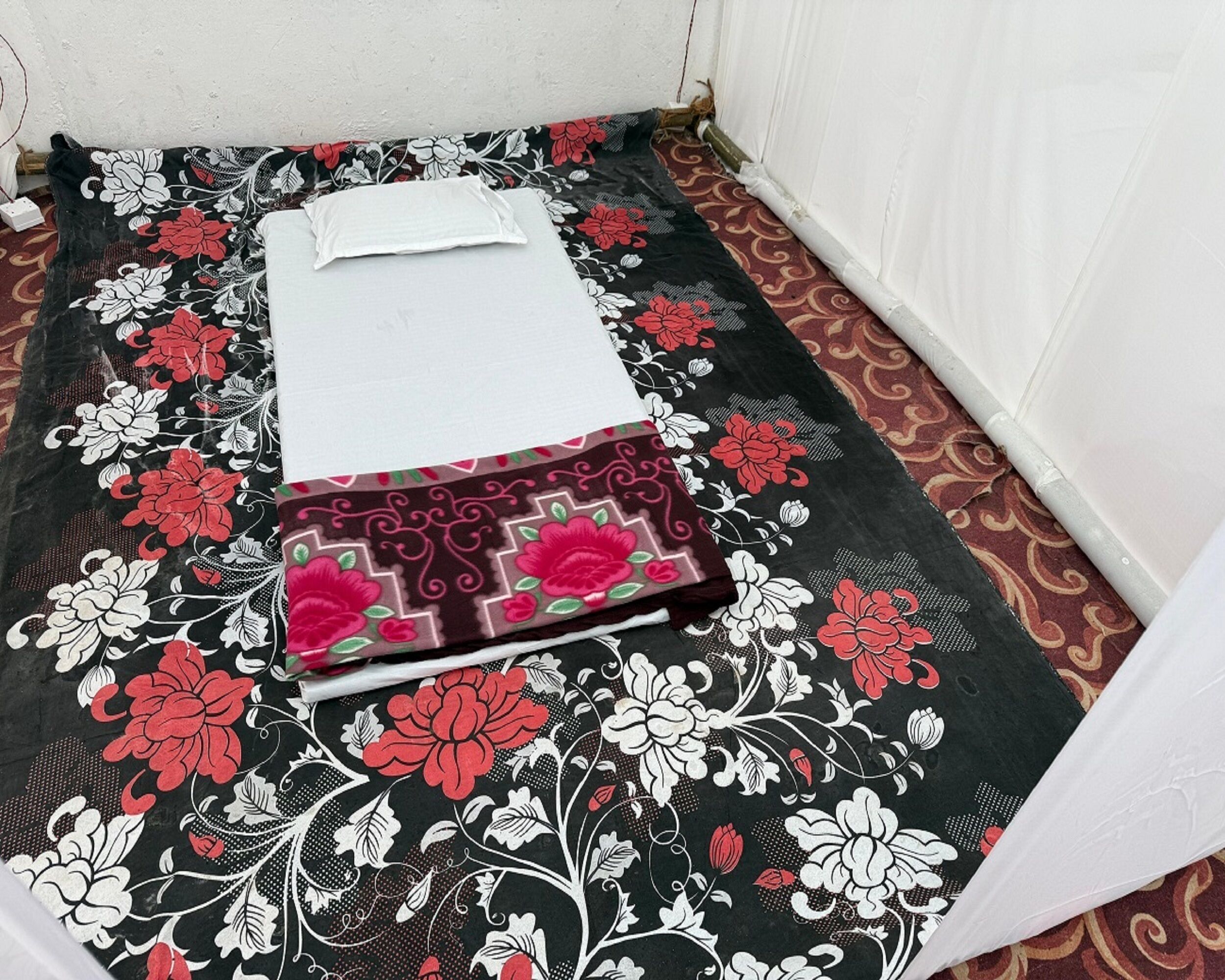 Una habitación pequeña con una cama individual, una colcha de estampado floral y una almohada blanca.
