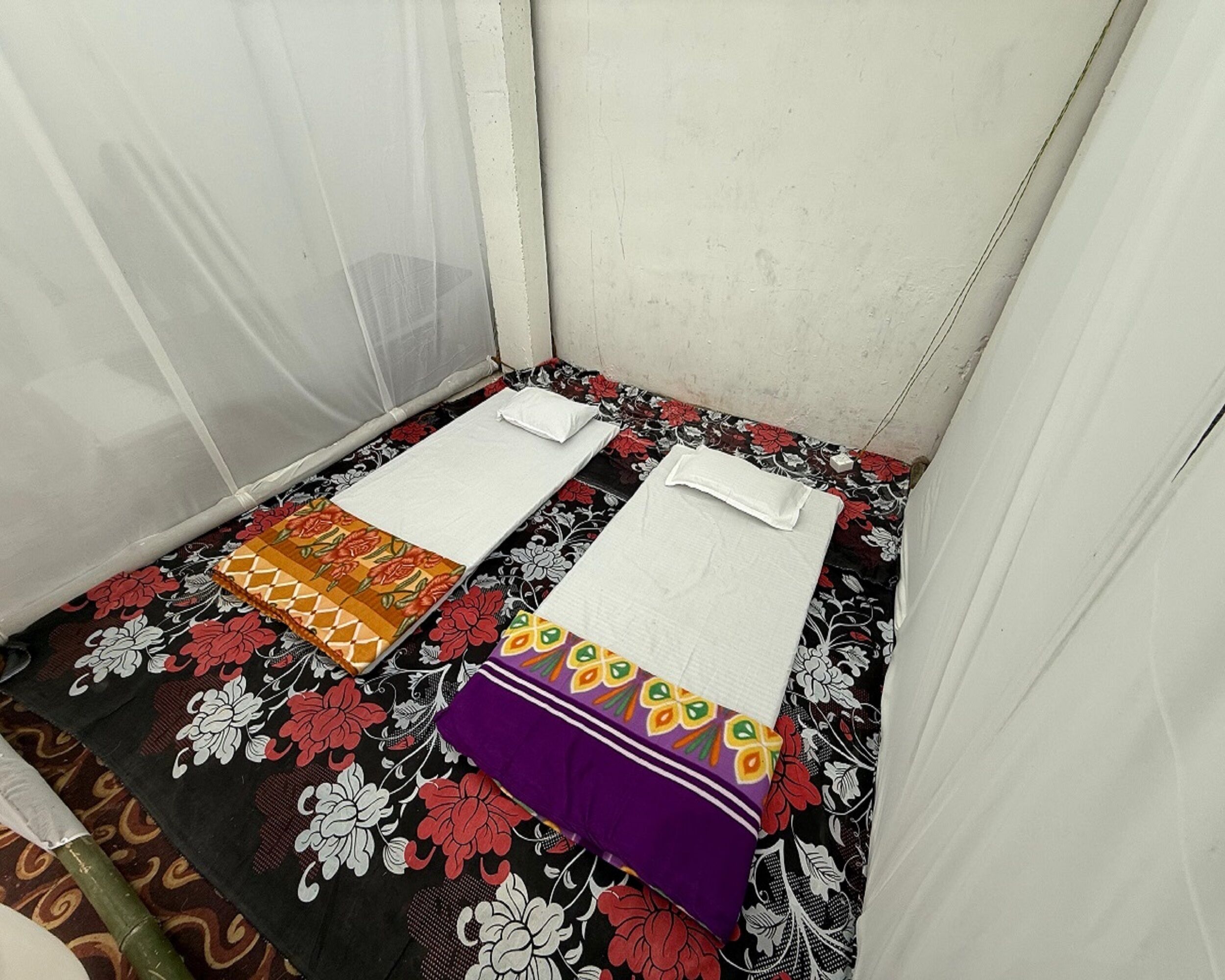 Een kleine, afgesloten kamer met twee bedden, elk met een bloemenprintdeken en witte kussens.