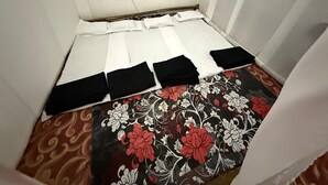 Una habitación pequeña y estrecha con una cama pegada a la pared, una alfombra estampada y una cortina blanca.